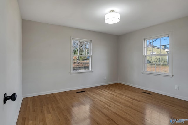 unfurnished room featuring a healthy amount of sunlight, visible vents, and wood finished floors