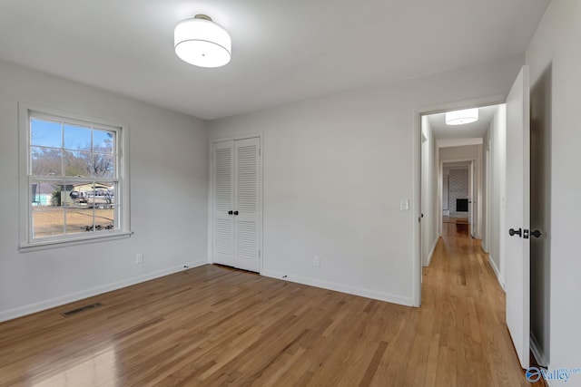 unfurnished bedroom with light wood-style flooring, a closet, visible vents, and baseboards