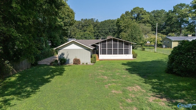 back of house featuring a sunroom, a fenced backyard, a wooded view, and a lawn