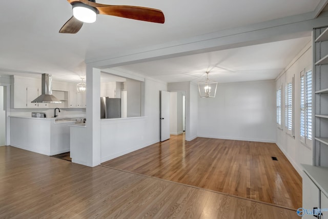 interior space with visible vents, baseboards, wood finished floors, a sink, and ceiling fan with notable chandelier