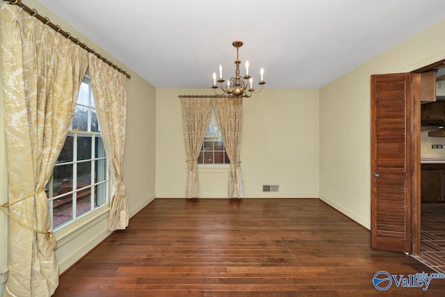 unfurnished dining area with a notable chandelier and dark wood-type flooring