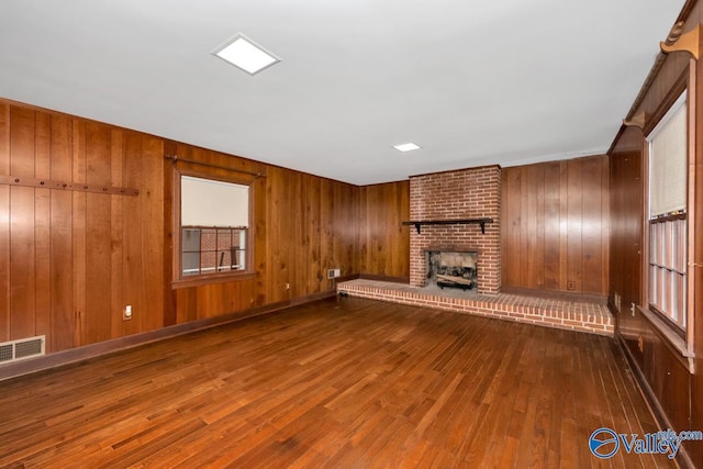 unfurnished living room with a fireplace, hardwood / wood-style floors, and wooden walls