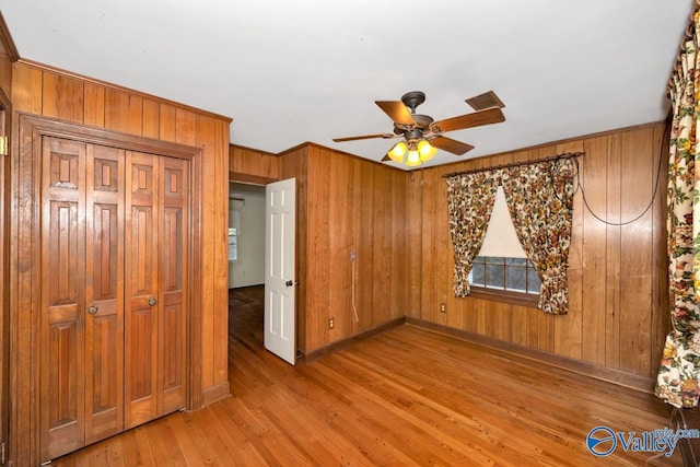 unfurnished bedroom with ceiling fan, wooden walls, and light wood-type flooring