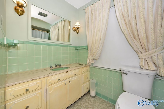 bathroom with vanity, toilet, and tile walls