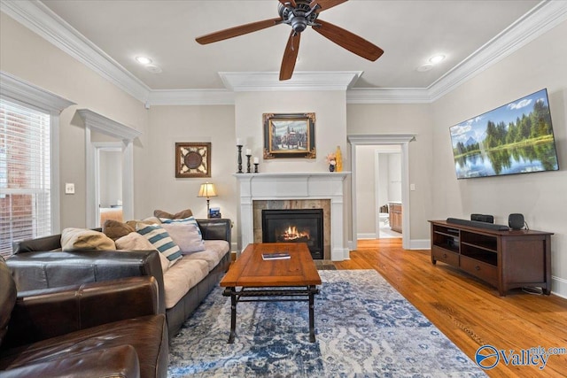 living area featuring baseboards, ceiling fan, wood finished floors, crown molding, and a fireplace