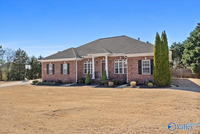 view of front of house featuring roof with shingles, fence, and brick siding