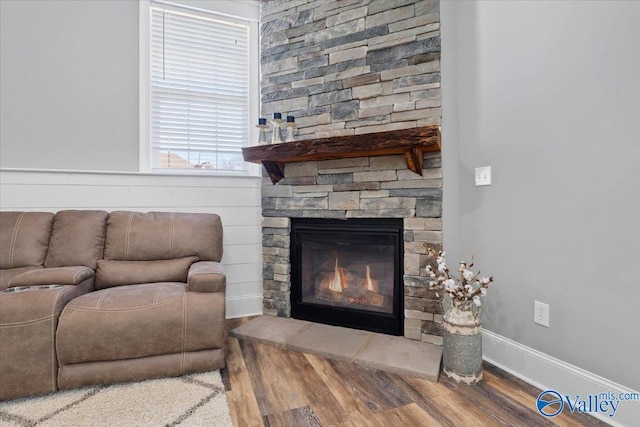 living room with a stone fireplace, wood finished floors, and baseboards