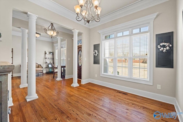 unfurnished dining area with baseboards, visible vents, wood finished floors, crown molding, and ornate columns