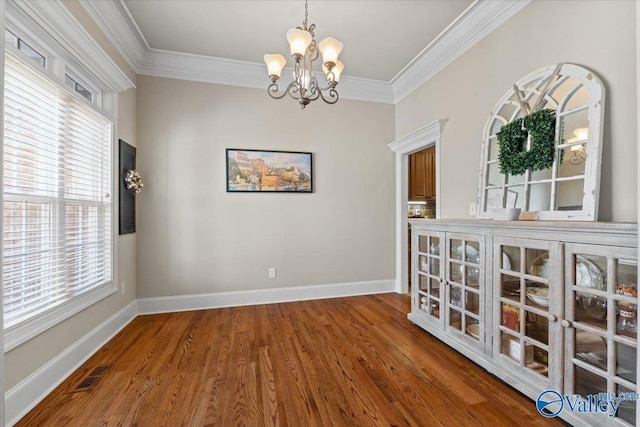 spare room featuring baseboards, visible vents, wood finished floors, and ornamental molding