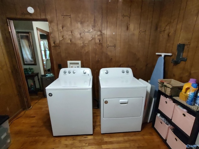 clothes washing area with wood-type flooring, wooden walls, and washing machine and dryer