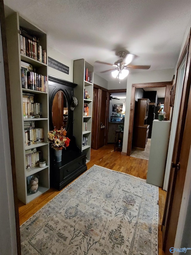 interior space with a textured ceiling, ceiling fan, and light hardwood / wood-style flooring