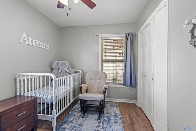 bedroom with a nursery area, dark hardwood / wood-style flooring, ceiling fan, a textured ceiling, and a closet