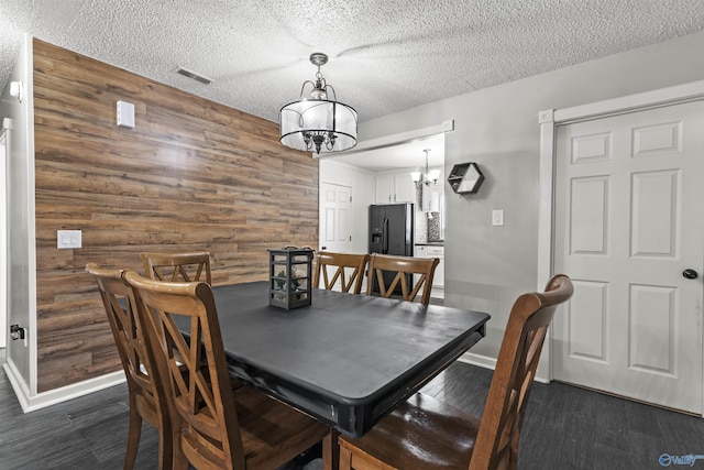 dining area with an inviting chandelier, dark wood-type flooring, wooden walls, and a textured ceiling