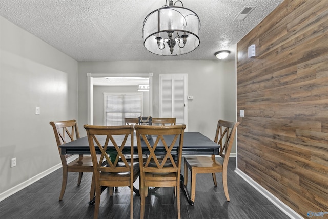 dining space featuring a chandelier, wooden walls, dark hardwood / wood-style flooring, and a textured ceiling