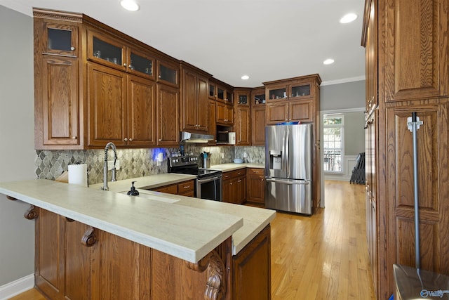 kitchen featuring ornamental molding, a sink, under cabinet range hood, appliances with stainless steel finishes, and a peninsula