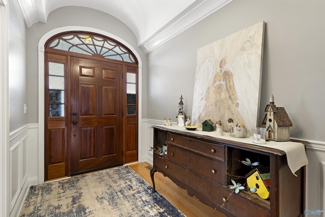 foyer entrance featuring a wainscoted wall, a decorative wall, light wood-style flooring, and vaulted ceiling
