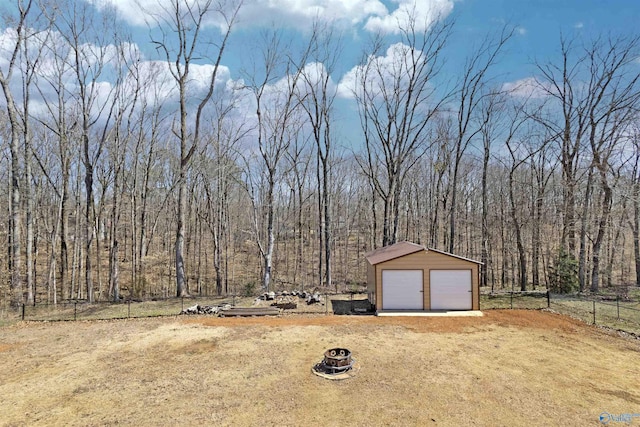 view of yard featuring an outbuilding, a wooded view, a detached garage, and fence