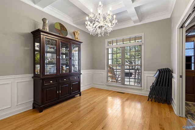 dining space with a wainscoted wall, coffered ceiling, beam ceiling, light wood-style flooring, and a chandelier