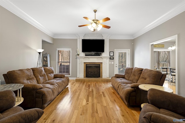 living room featuring a tiled fireplace, ceiling fan, light wood-style floors, and ornamental molding