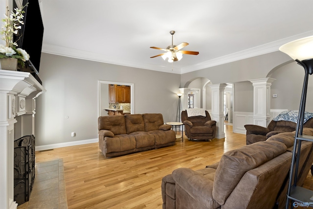 living room featuring arched walkways, light wood-style flooring, a ceiling fan, and ornate columns