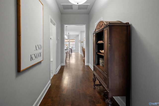 hallway featuring dark wood-type flooring, visible vents, and baseboards