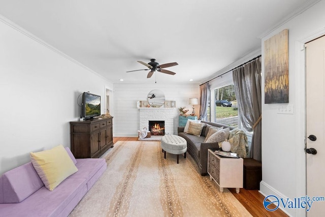 living area with light wood-type flooring, ornamental molding, a ceiling fan, a warm lit fireplace, and baseboards