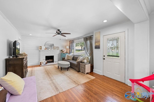 living room with wood finished floors, recessed lighting, a fireplace with raised hearth, ceiling fan, and crown molding