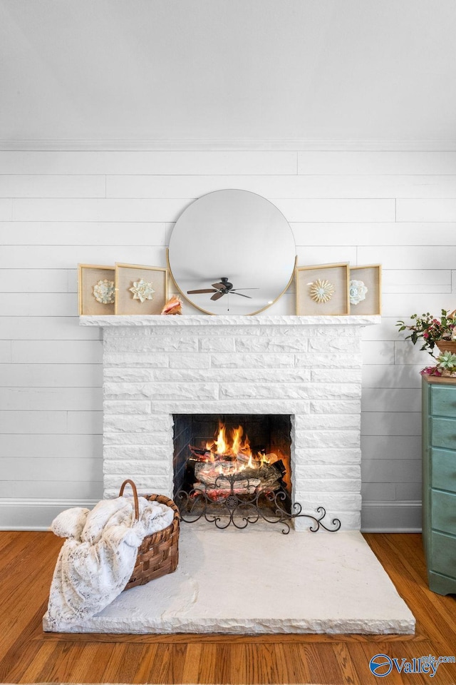 details with a ceiling fan, wood finished floors, wooden walls, a fireplace, and baseboards