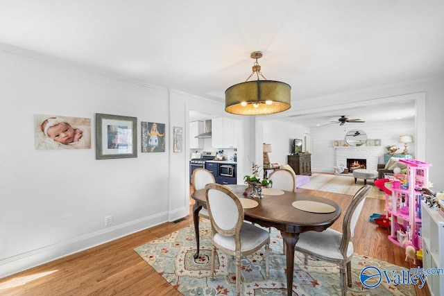 dining space featuring a ceiling fan, baseboards, a fireplace, crown molding, and light wood-type flooring