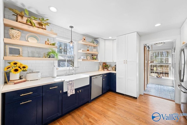 kitchen featuring blue cabinetry, open shelves, light wood-style flooring, stainless steel appliances, and a sink