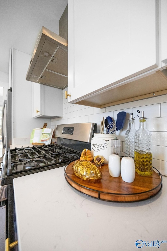 interior details featuring stainless steel gas range oven, tasteful backsplash, white cabinets, and wall chimney range hood