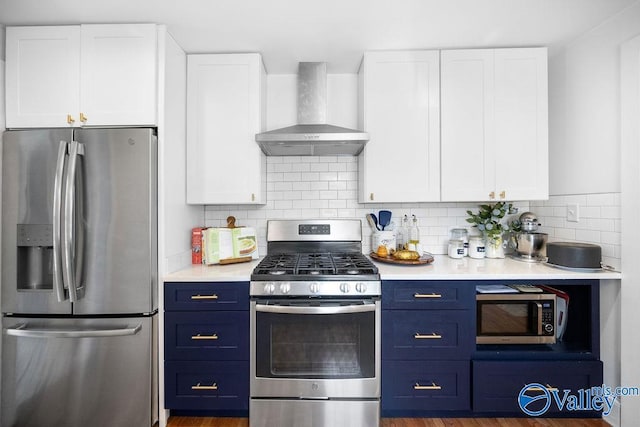 kitchen with blue cabinetry, stainless steel appliances, wall chimney exhaust hood, and white cabinetry