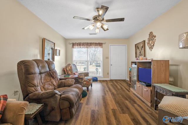 living room with a textured ceiling, ceiling fan, and dark wood-type flooring