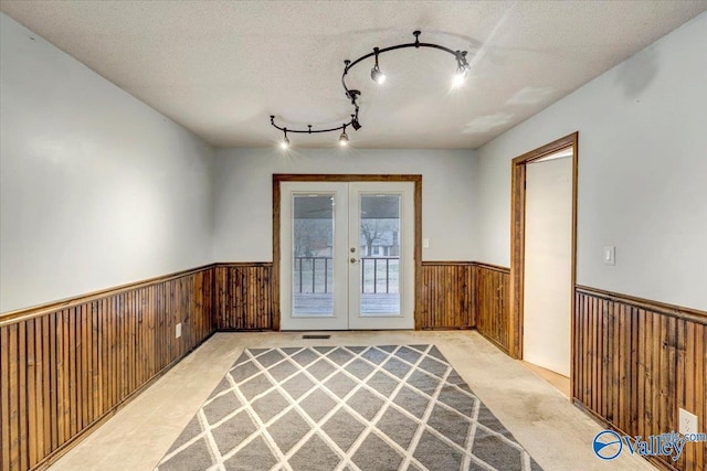 unfurnished room with french doors, light colored carpet, track lighting, and a textured ceiling