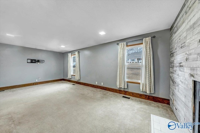 unfurnished room with a healthy amount of sunlight, light colored carpet, and a fireplace