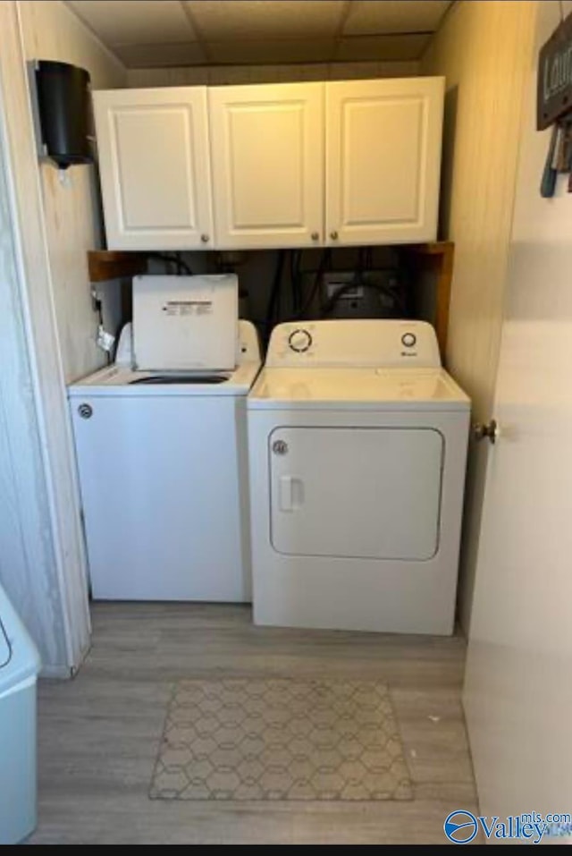 laundry area featuring light hardwood / wood-style floors, washing machine and dryer, and cabinets