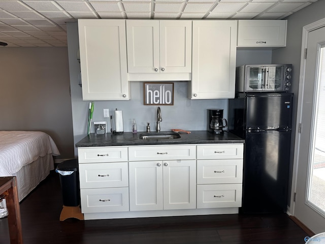 kitchen featuring a drop ceiling, sink, white cabinets, and black fridge