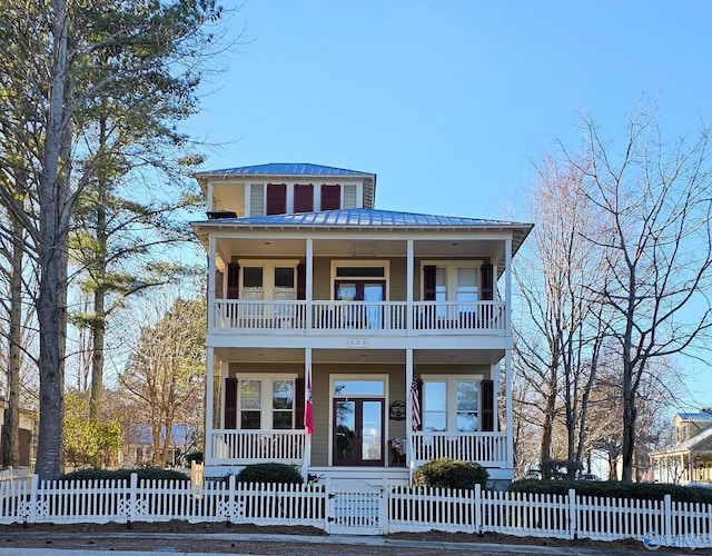 view of front of home with a balcony, a fenced front yard, metal roof, covered porch, and a standing seam roof