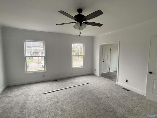 carpeted empty room featuring crown molding, a ceiling fan, visible vents, and baseboards