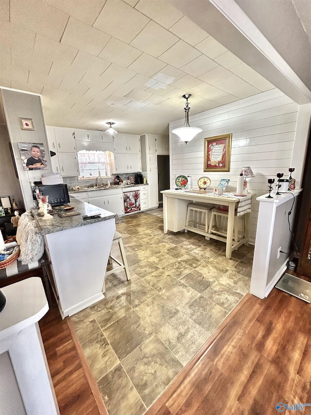 kitchen featuring black microwave, a peninsula, white cabinetry, wood walls, and a sink