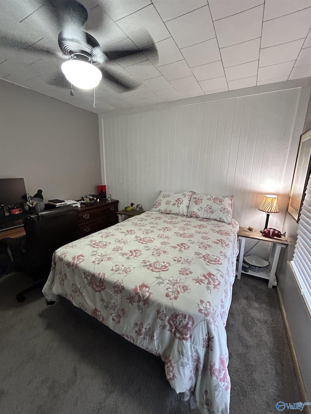 bedroom with wood walls, ceiling fan, and dark colored carpet