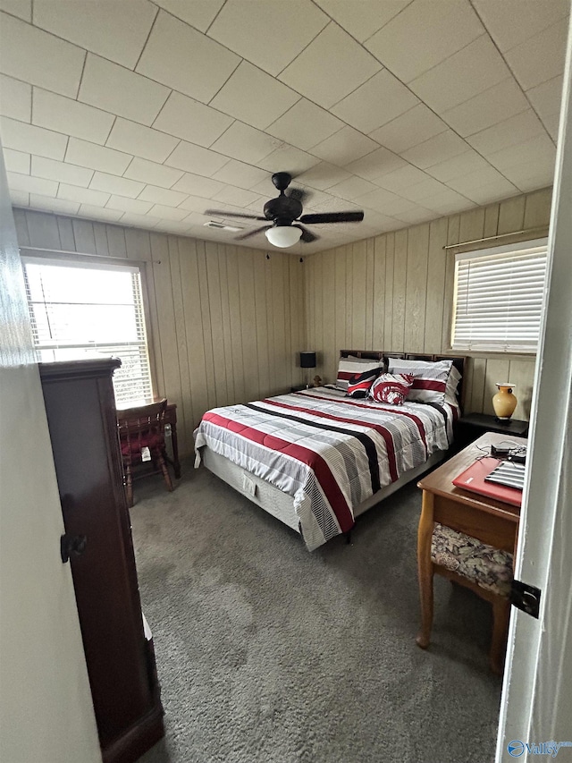 carpeted bedroom with wooden walls, ceiling fan, and multiple windows