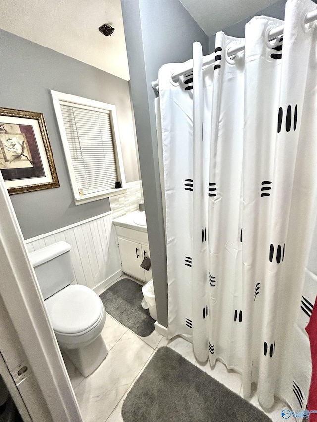 full bath featuring tile patterned flooring, toilet, curtained shower, and wainscoting