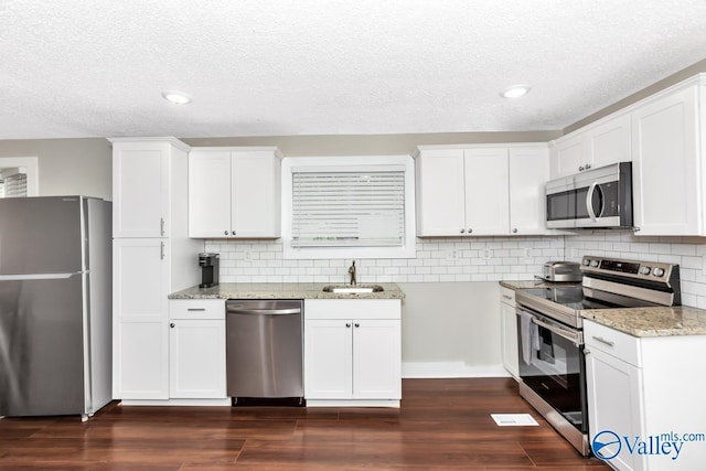 kitchen featuring a textured ceiling, a sink, appliances with stainless steel finishes, light stone countertops, and dark wood-type flooring
