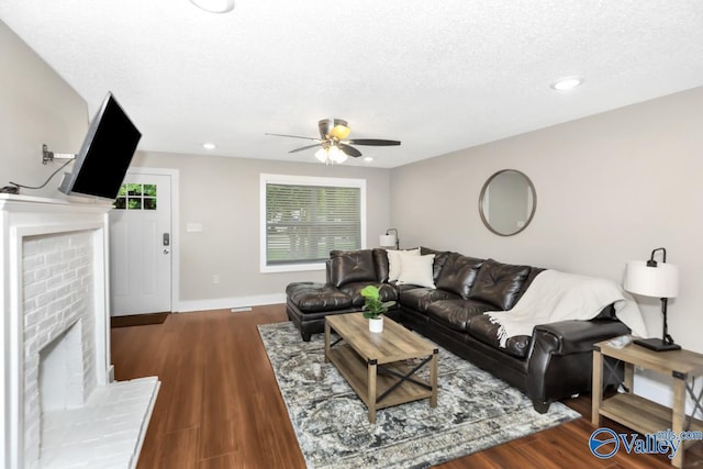 living area featuring a ceiling fan, wood finished floors, a textured ceiling, baseboards, and a brick fireplace