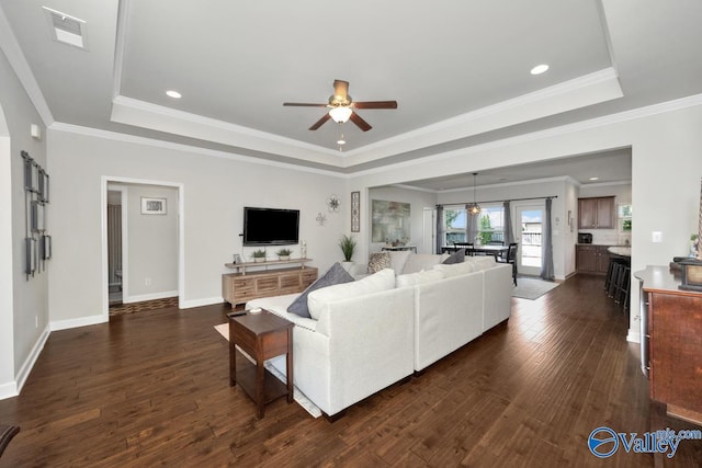 living room featuring dark hardwood / wood-style flooring, ornamental molding, a raised ceiling, and ceiling fan