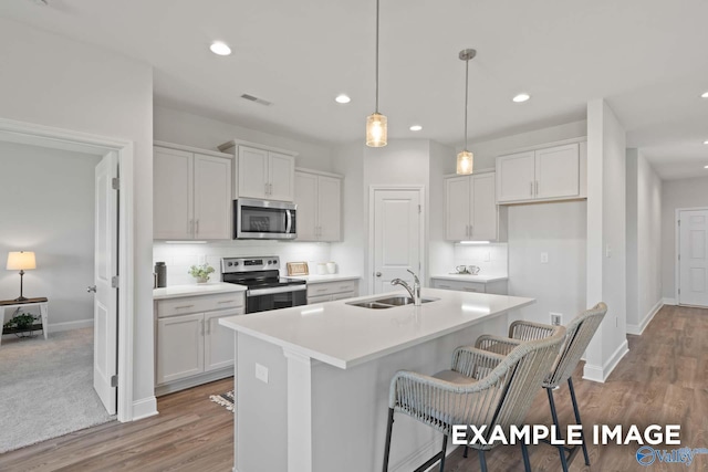 kitchen with appliances with stainless steel finishes, a center island with sink, white cabinetry, and sink