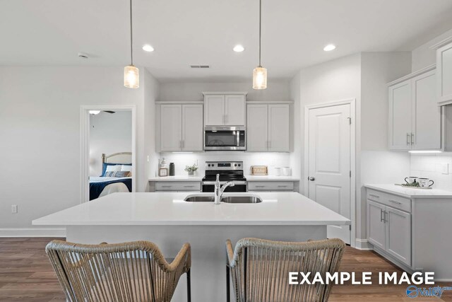 kitchen featuring decorative light fixtures, stainless steel appliances, dark wood-type flooring, and an island with sink