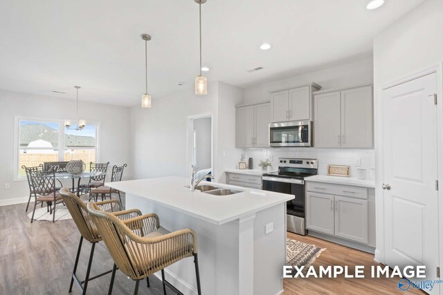 kitchen featuring a kitchen island with sink, sink, decorative light fixtures, light hardwood / wood-style floors, and stainless steel appliances