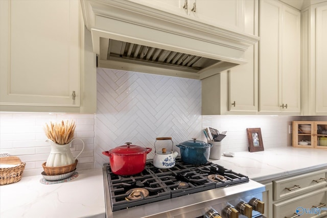 kitchen with custom exhaust hood, light stone countertops, tasteful backsplash, range, and stainless steel gas cooktop